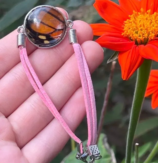 Hand holds pink bracelet with butterfly design near bright orange flower.